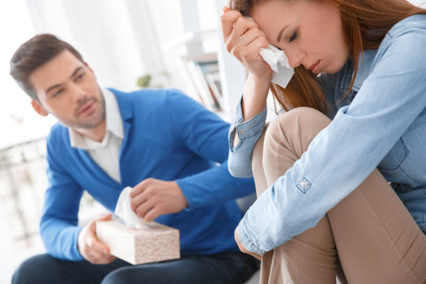 Young couple waiting for psychology session family problems girl crying Young couple man and woman waiting for psychology session sitting on sofa girl crying depressed close-up boyfriend giving her tissue to calm down wiping tears stock pictures, royalty-free photos & images