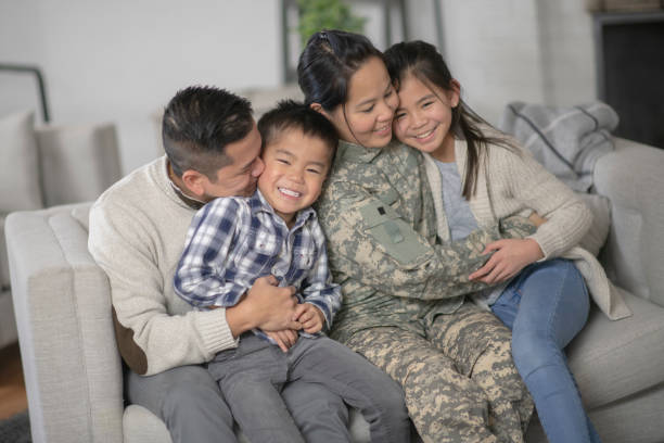 Military Family Sitting On Couch A family of four is happily sitting on the sofa in their living room. The mother has just returned home from serving her country and is wearing a military uniform. filipino family reunion stock pictures, royalty-free photos & images