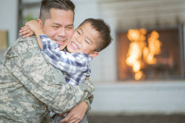 Welcoming Dad Home A military dad and his son are hugging in their living room. The son is running up to the father and jumping into his arms while smiling. filipino family reunion stock pictures, royalty-free photos & images