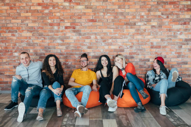 millennials chilling out leisure zone laughing Millennials chilling out in leisure zone after successful hard working day. Young people sitting in cushion chair, laughing. people laughing hard stock pictures, royalty-free photos & images