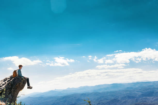Man sitting on the edge of a cliff overlooking the mountains below