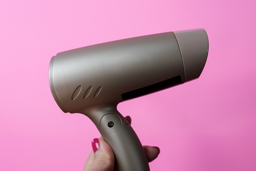 Closeup of woman's hand holding rose gold travel size blow dryer