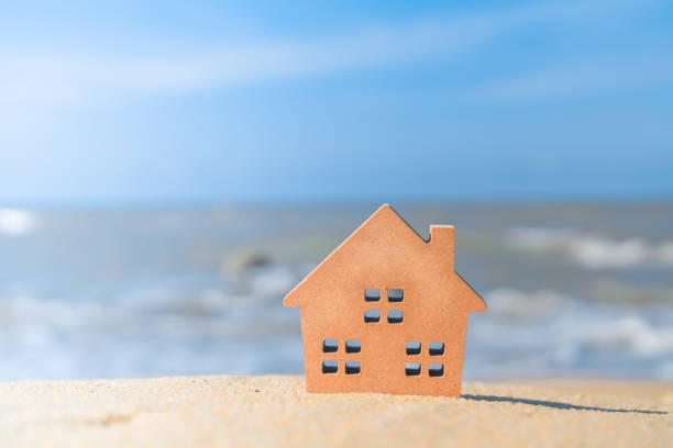 istock Closed up tiny home models on sand with sunlight and beach background. 1143172108