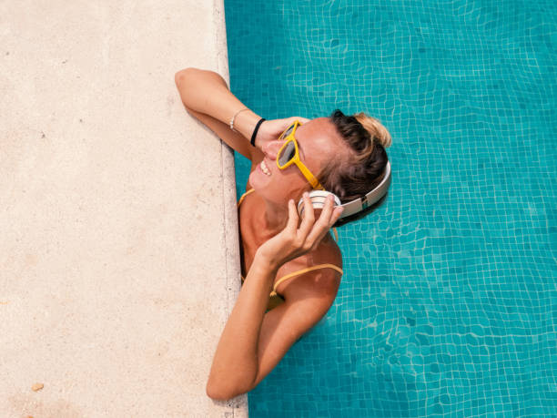 feliz mujer joven relajante en la piscina y escuchando música con auriculares inalámbricos - swimwear bikini swimming pool red fotografías e imágenes de stock