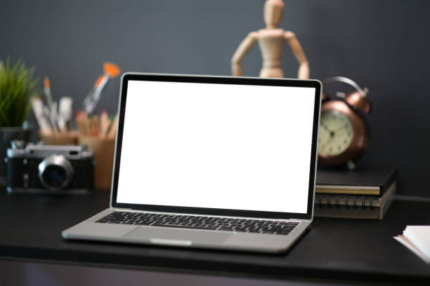 istock Stylish dark desk with blank screen laptop mock up 1143177640