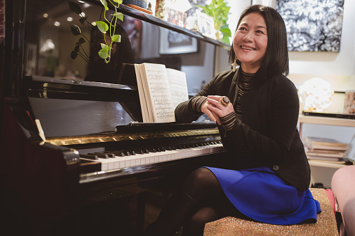 Chinese joyful mature woman sitting at piano at apartment, smiling happily