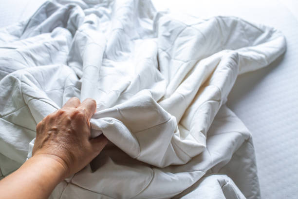 istock Woman's hand picking up white crumpled bed sheet on white bed, Close up shot, Selective focus, Bedroom cleaning concept 1143186635
