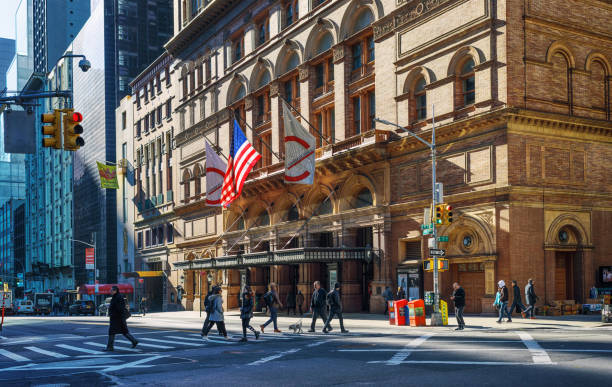 01 April 2019: Carnegie Hall is a concert venue in Midtown Manhattan in New York City, United States, located at Seventh Avenue. Manhattan is world’s major commercial, financial and cultural center and the most densely populated of New York City’s 5 boroughs. Local people are crossing the street.