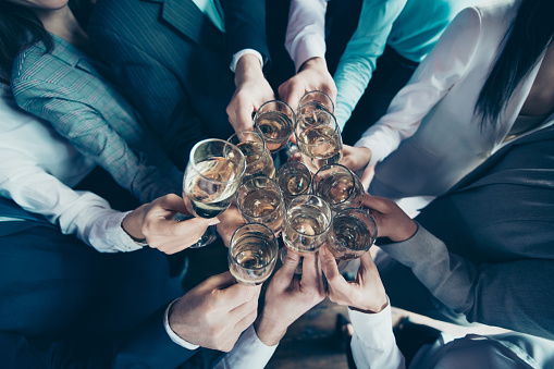 Cropped top above high angle view close up photo business people diversity age race team members she her he him his hold hands arms clink golden wine say toasts congrats formal wear jackets shirts.