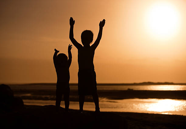 Children standing on beach at sunset.