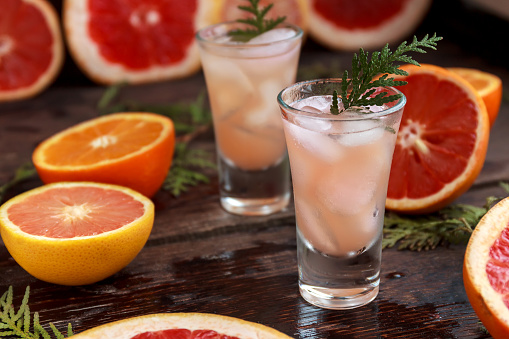 fresh grapefruits and citrus sliced and a tall glass filled with juice and alcohol with ice on wooden table