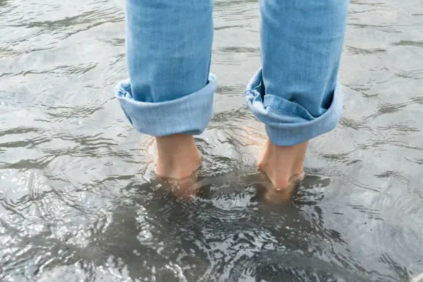 feet of a woman  wearing blue jeans in cold river water during a Kneipp footbath