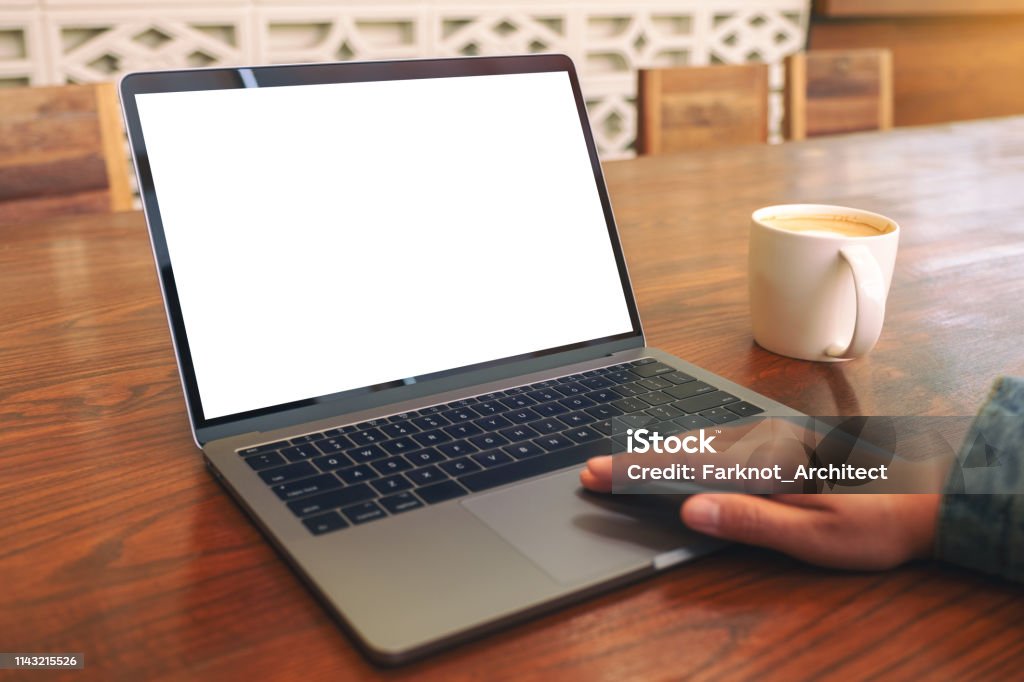 a woman's hand using and touching on laptop touchpad with blank white desktop screen Mockup image of a woman's hand using and touching on laptop touchpad with blank white desktop screen with coffee cup on wooden table Above Stock Photo