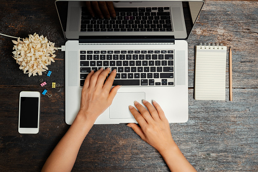 Close up hands of businesswoman working on computer notebook with samart phone and others stationery  on vintage wooden table,top view.