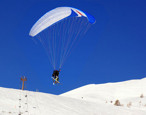 Double ski paragliding in the mountains in winter on blue sky background.