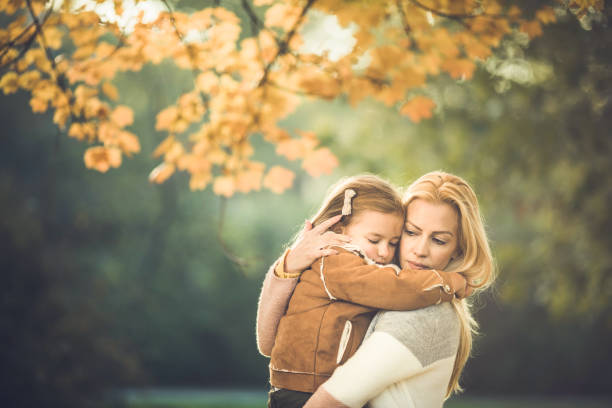 Affectionate mother consoling her little girl during autumn day in nature.