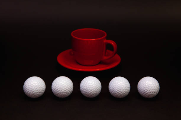 istock White golf balls and red cup of tea on the black table. 1143228043