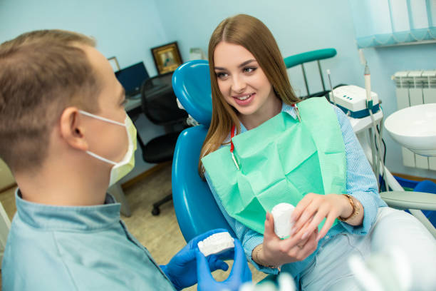 uma menina está sentando-se na cadeira dental e está olhando um doutor do homem que esteja falando a ela. clínica odontológica - tranquilizing - fotografias e filmes do acervo