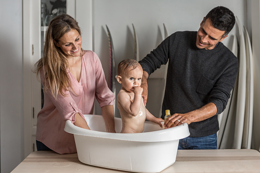 Parents together bathe the baby in the bathtub at home