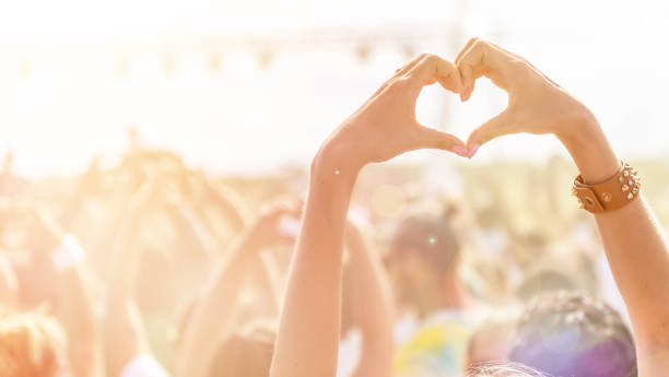 Woman making a heart-shape symbol for her favorite band at music festival.