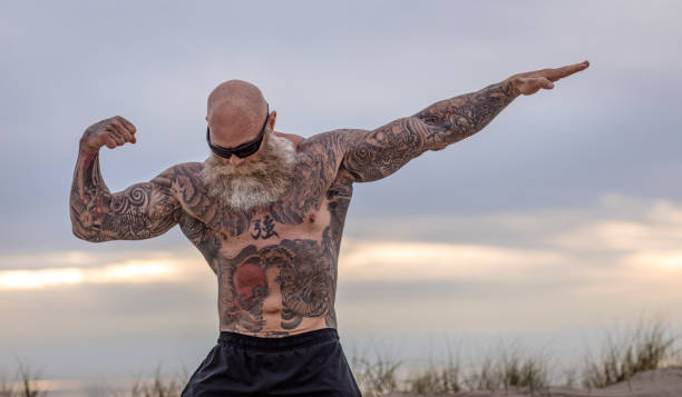 Tattooed Senior Man During Workout Bearded Aggressive Senior Man during workout on a beach senior bodybuilders stock pictures, royalty-free photos & images