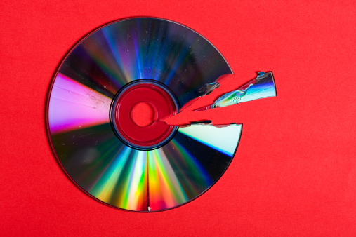 CD or DVD with a ragged sliver broken out of it. Red background. Camera: Canon EOS 1Ds Mark III. 