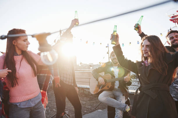 istock Dancing in sunshine. Group of young people having celebration at a rooftop with some alcohol and guitar playing 1143234977