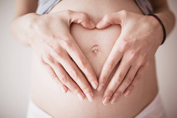 A close-up of a pregnant woman holding a heart plushie toy over her stomach.
