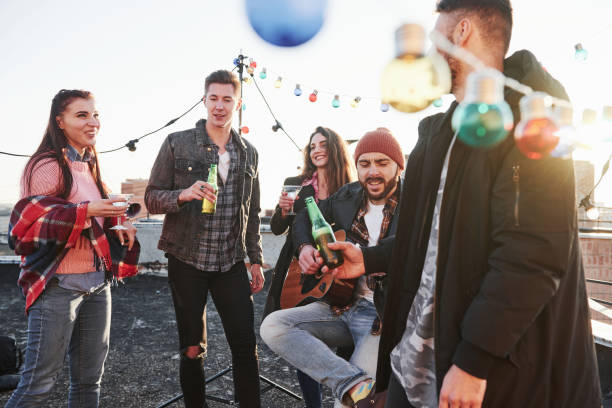 istock Good weekend. Rooftop party. Friends with alcohol having good time. Guy playing guitar 1143235936