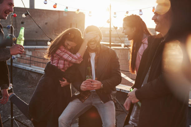 Awesome sunshine. Young couple having fun with friends on the rooftop. Girl covers guy's face Awesome sunshine. Young couple having fun with friends on the rooftop. Girl covers guy's face. man with a light bulb over his head stock pictures, royalty-free photos & images
