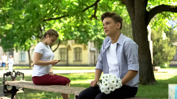 nastolatek waha się przedstawić kwiaty dziewczynie w parku, pani za pomocą smartfona - hesitating zdjęcia i obrazy z banku zdjęć