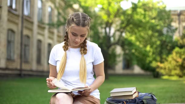istock Young woman reading book on bench on campus, preparing homework, education 1143238481