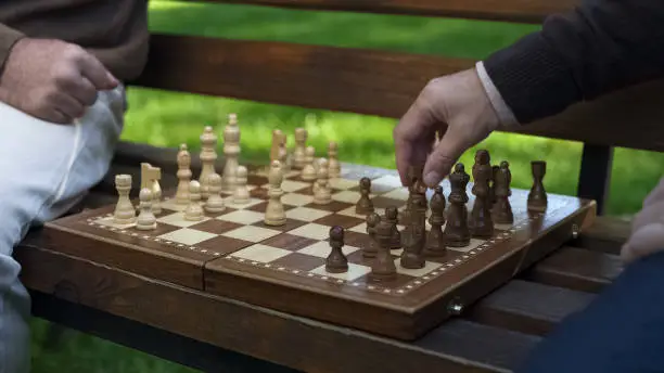 Grandfathers playing chess on bench, moving figures on board, game beginning