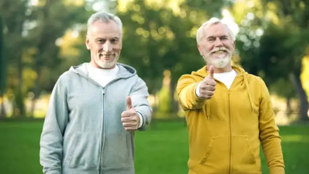 Two smiling elderly men in sportswear showing thumbs up, healthy lifestyle