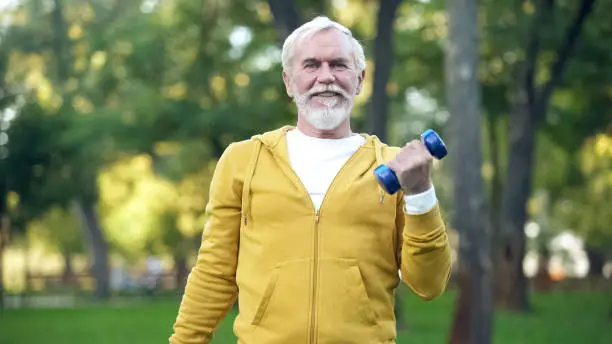 Handsome aged man doing arm exercises with dumbbells in park, leisure activity