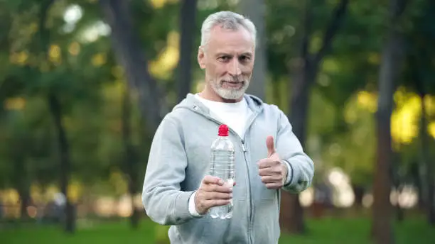 Senior man in sportswear showing bottle of water and thumbs up, aqua balance