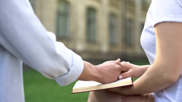 istock Couple holding hands, woman reading book, choice between study and relations 1143239248
