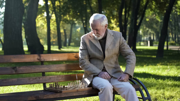 istock Mature man preparing chessboard for game sitting on bench in park, retirement 1143239299