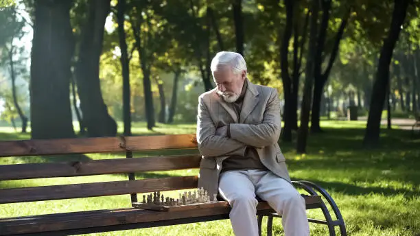 Old thoughtful man playing chess in park alone, social security for pensioners