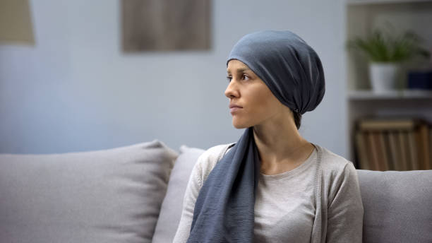 Upset young lady in headscarf lonely sitting on sofa in oncologic hospital Upset young lady in headscarf lonely sitting on sofa in oncologic hospital colorectal cancer photos stock pictures, royalty-free photos & images