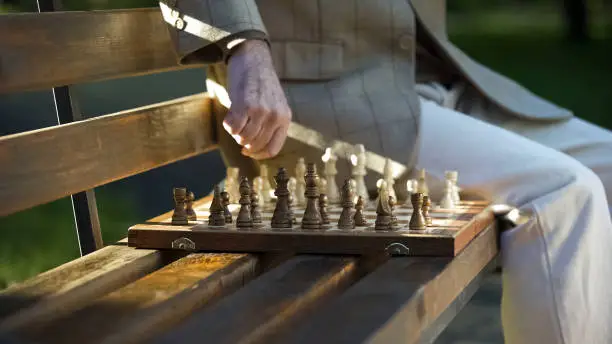 Old man resting and playing chess alone in park, retirement benefits, close up