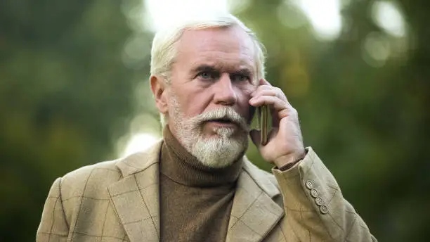 Serious elderly businessman talking on phone, bad news, communication technology