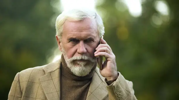 Confident mature man talking on phone, listening to opponent, communication