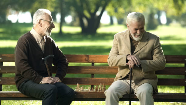 istock Old friends sitting on bench in park and remembering young years, playing chess 1143239639