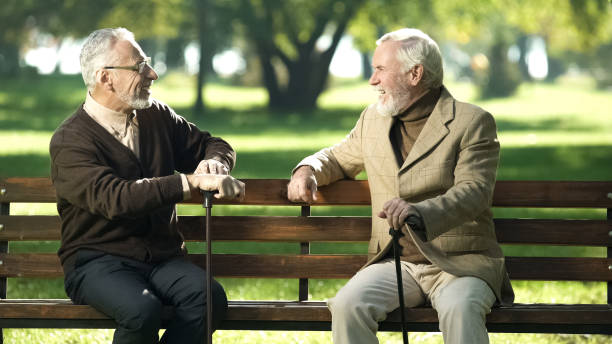 istock Aged male friends with walking sticks resting on bench in park and talking 1143239655