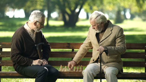 Old friends sitting on bench in park and playing chess, happy leisure time Old friends sitting on bench in park and playing chess, happy leisure time senior chess stock pictures, royalty-free photos & images
