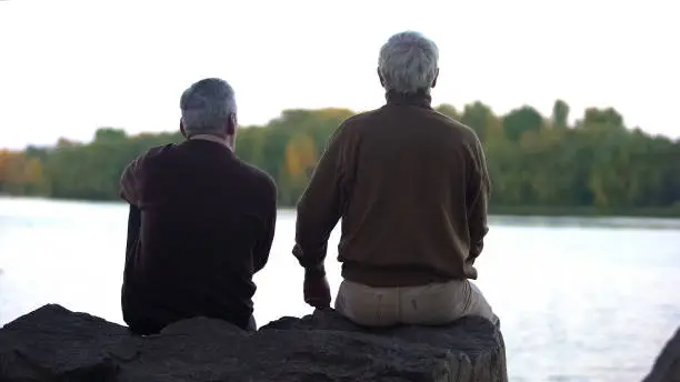 Elderly pensioners enjoying forest and water sitting on river bank, weekend rest
