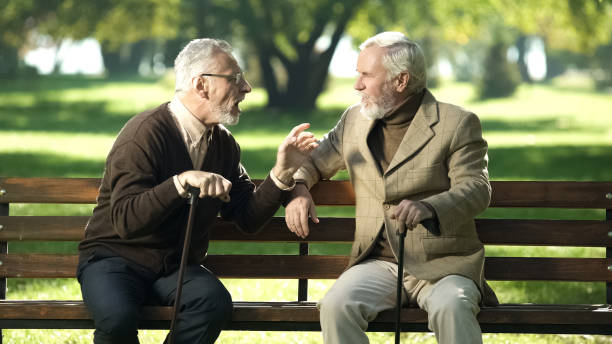 istock Gray friends spending time on bench in park breathing fresh air and talking 1143239749