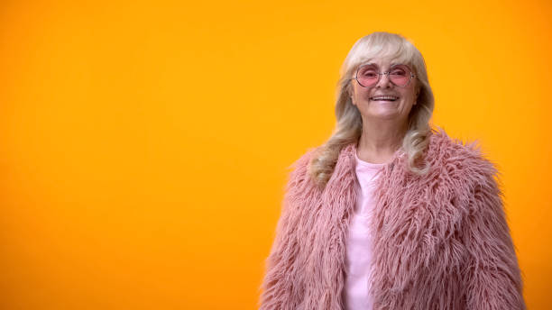 istock Cheerful retiree lady in funny pink coat and round sunglasses posing on camera 1143240036