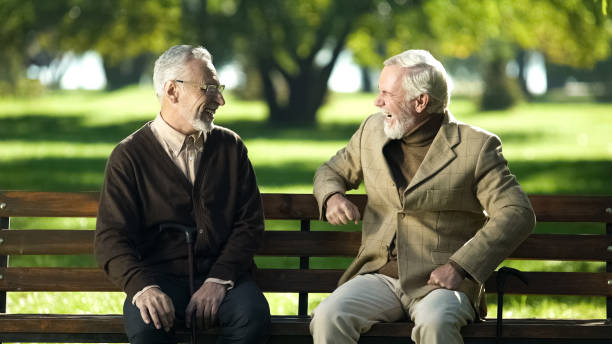 istock Two senior people laughing remembering young years sitting on bench in park 1143240039